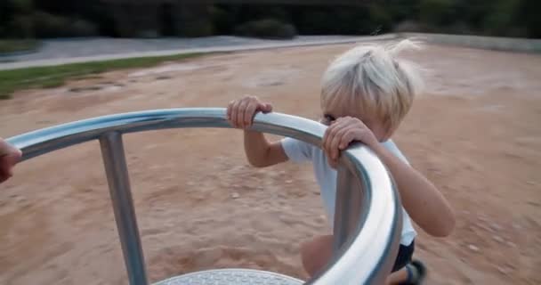 Šťastné dítě na hřišti točí na kolotoči houpačka a směje se při západu slunce — Stock video