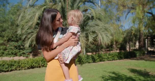 Mooie moeder en schattig dochtertje praten in een groen tropisch park — Stockvideo