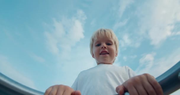 Счастливый ребенок на детской площадке крутится на карусели и смеется на закате — стоковое видео