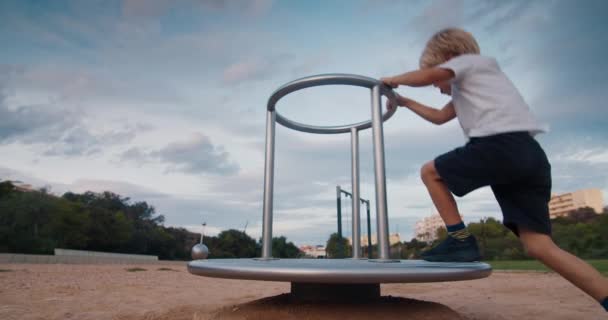 Happy child on playground spinning on carousel swing and laughing on sunset — Stock Video