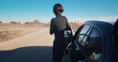 Genç ve güzel bir kadın arabadan iniyor ve uyarı üçgeni çiziyor. 