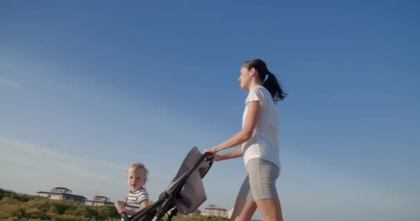Zamknij się młoda kobieta spacery z dzieckiem w wózku na tle nieba — Wideo stockowe