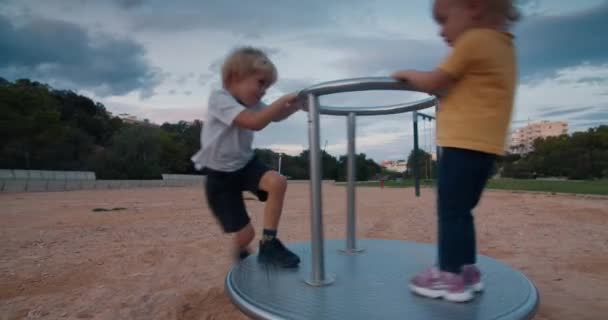 Crianças felizes girando no balanço do carrossel e rindo no pôr do sol — Vídeo de Stock