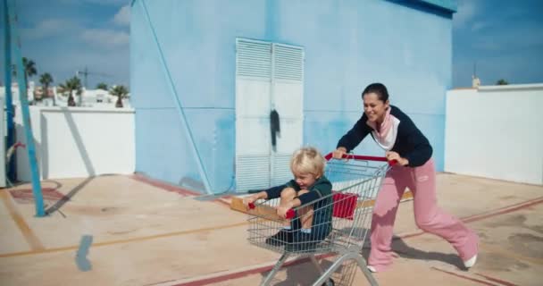 Молодая счастливая мать бегает с тележкой с ребенком, сидящим в ней на парковке — стоковое видео