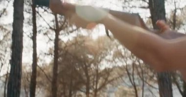 Uzun saçlı, genç ve çekici bir kadın ormanda tüfek ve ateş yakıyor.