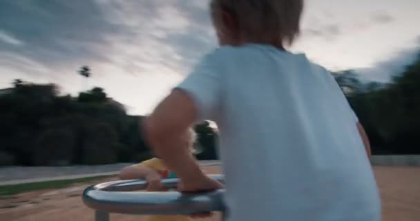 Niños felices girando en carrusel swing y riendo al atardecer — Vídeo de stock