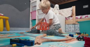 Çocuk odasında tahta demiryolu oyuncağıyla oynayan sevimli, mutlu çocuk.