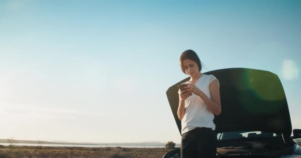 道路上のスマートフォン通話サービスを使用して故障車の前の若い女性 — ストック動画
