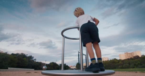 Счастливый ребенок на детской площадке крутится на карусели и смеется на закате — стоковое видео