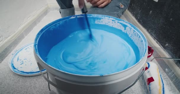 Primeros planos joven mano mezcla pintura azul en cubo — Vídeo de stock