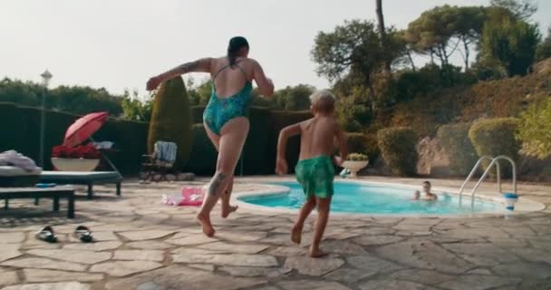 Молодая женщина бежит с детьми и прыгает в бассейн — стоковое видео