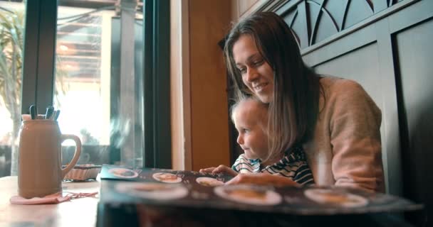 Wanita muda dengan bayi perempuan di restoran menonton menu memilih makanan — Stok Video