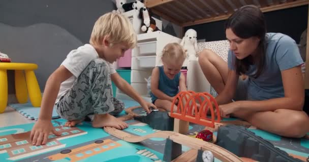 Felice madre di famiglia con bambini che giocano strada ferroviaria in legno nella stanza dei bambini — Video Stock