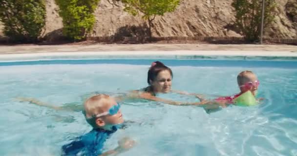 Молодая женщина с детьми плавает в бассейне на летних каникулах — стоковое видео