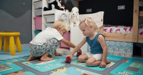 Lindo niño pequeño con hermana jugando con camión de bomberos de juguete en el dormitorio del niño en casa — Vídeos de Stock