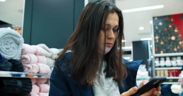 Junge schöne Frau benutzt Handy beim Einkaufen im Geschäft und setzt Gesichtsmaske auf — Stockvideo