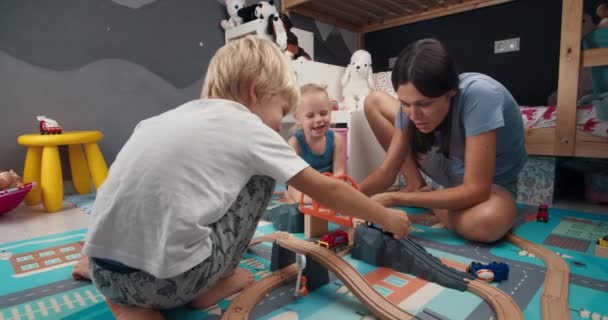 子供部屋で木製の鉄道道路を再生子供と幸せな家族の母親 — ストック動画