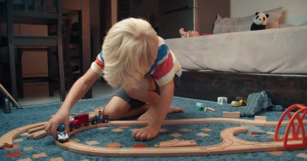 Χαριτωμένο χαρούμενο αγόρι παίζει ξύλινο σιδηροδρομικό παιχνίδι στο σαλόνι το βράδυ — Αρχείο Βίντεο