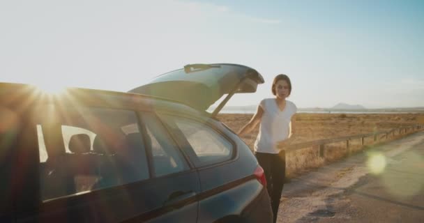 Chica en la luz del sol cerrando el maletero del coche y se pone al volante para continuar viaje — Vídeos de Stock