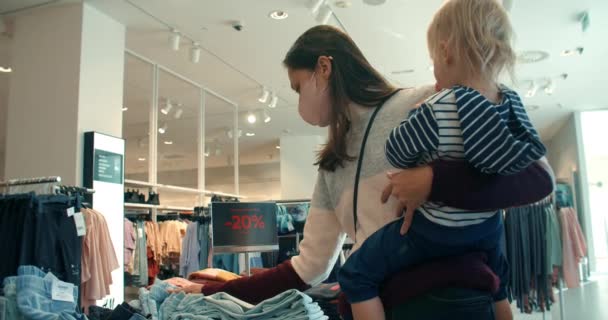 Νεαρή όμορφη γυναίκα με κόρη ψώνια με εκπτώσεις κλείσιμο νέα ρούχα — Αρχείο Βίντεο