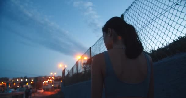 Junge Frau mit Kinderwagen läuft abends im Urlaub am Maschendrahtzaun entlang — Stockvideo