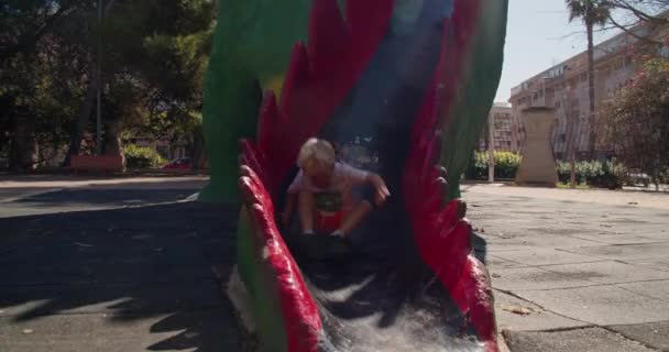 Щаслива дитина спускається на високий дитячий слайд дракона і біжить в літній день — стокове відео