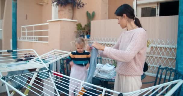 Młoda kobieta z córką dziewczynka wisi mokre pranie na zewnątrz — Wideo stockowe