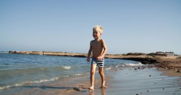 Niño feliz corriendo y sonriendo en la playa frente al mar en las vacaciones de verano — Vídeo de stock