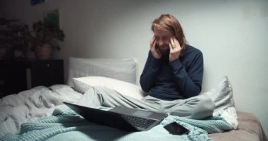 Kanepede oturup dizüstü bilgisayarla çalışan kendini kötü hisseden bir adam.