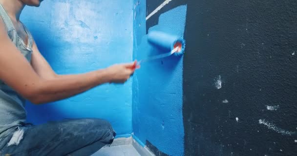 Attraente giovane donna pittura muro nero su blu con rullo — Video Stock