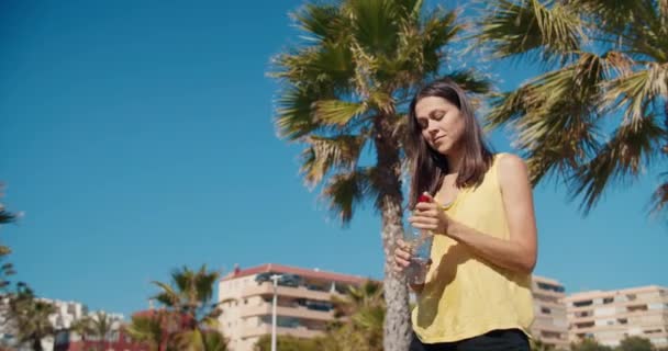 Jeune femme attrayante boit de l'eau de bouteille en plein air verser sur lui-même — Video