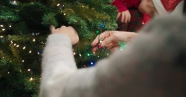 Genç kadın elleriyle Noel ağacını süslüyor ve çelenk ışıkları takıyor.