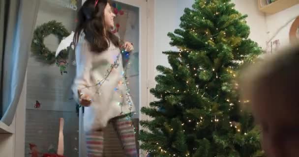 Χαρούμενη παιχνιδιάρικη οικογένεια στολίζει χριστουγεννιάτικο δέντρο, χορεύει μαζί μαμά και παιδιά — Αρχείο Βίντεο