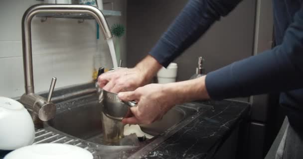 Чоловік крупним планом миє посуд на кухні, допомагаючи дружині — стокове відео
