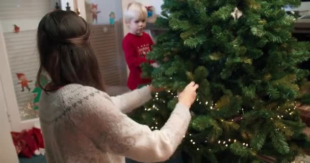 ผู้หญิงสาวตกแต่งต้นคริสต์มาสด้วยแสงและลูกชายของเธอ — วีดีโอสต็อก