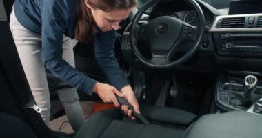 Aracın içini elektrikli süpürgeyle temizleyen genç bir kadın.