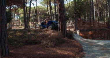 Sakallı, uzun saçlı ve oğlu ormanda dört tekerlekli bisiklet süren genç bir adam.