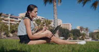 Serbest çalışan iş kadını yeşil çimlerde oturup düşünüyor ve dizüstü bilgisayarla çalışıyor.