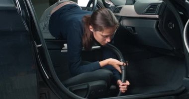 Aracın içini elektrikli süpürgeyle temizleyen genç bir kadın.