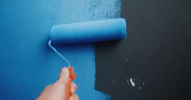Πρώτο πρόσωπο δείτε το χέρι άνθρωπος ζωγραφική μαύρο τοίχο σε μπλε χρησιμοποιώντας κύλινδρο — Αρχείο Βίντεο