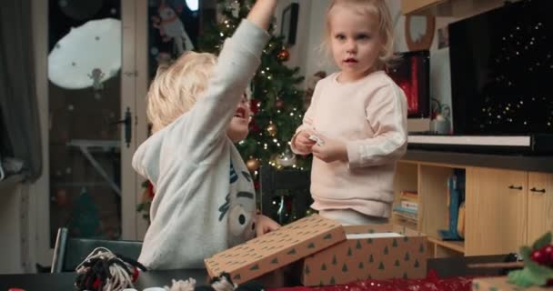 Παιχνιδιάρικα παιδιά πακετάρουν χειροποίητο Χριστουγεννιάτικο δώρο στο κουτί το βράδυ στο σπίτι — Αρχείο Βίντεο