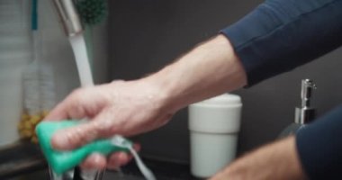 Erkek elleri yakın çekimde mutfakta bulaşık yıkıyor ve karısına yardım ediyor.