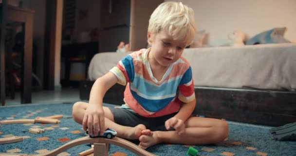 Child boy playing with toy car on wooden railway road in living room on evening – Stock-video