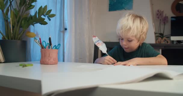 Akşam evde tüy kalemle boş kağıt üzerinde resim yapan çocuk. — Stok video