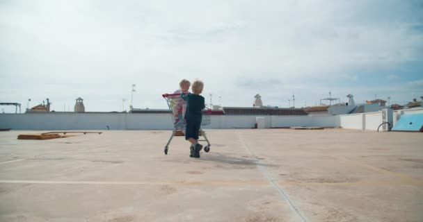 Kinderen hebben plezier spelen met supermarkt sopping kar in de buitenlucht parkeren — Stockvideo