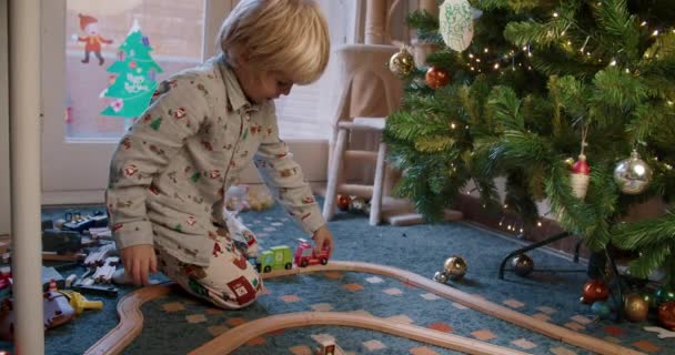 Ragazzo carino bambino che gioca con auto giocattolo su ferrovia stradale in legno vicino all'albero di Natale — Video Stock