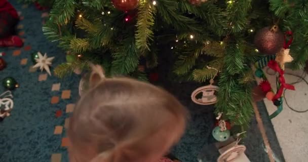 Nettes Baby-Mädchen schmückt Weihnachtsbaum zu Hause im Winterurlaub — Stockvideo