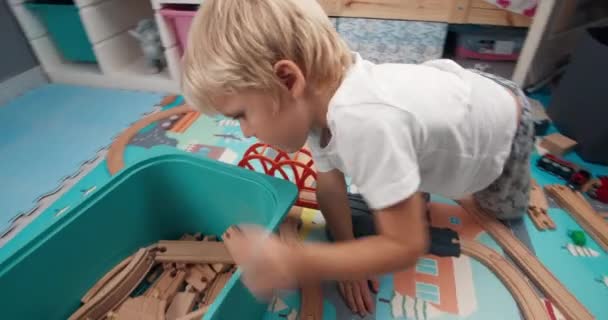 Милый игривый ребенок ищет деревянную дорожку в коробке для игрушек в спальне — стоковое видео