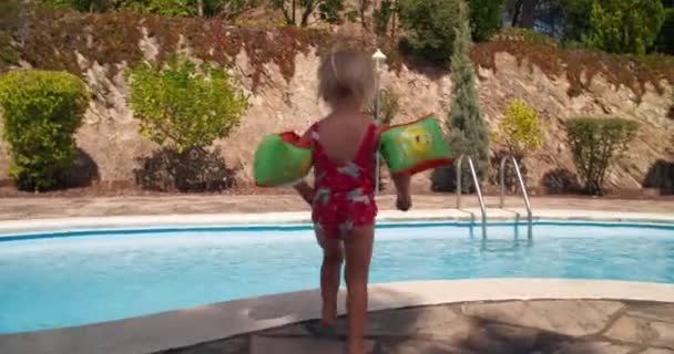Милая девочка, прыгающая в воду бассейна на летних каникулах — стоковое видео
