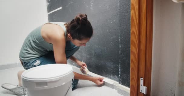 Young woman making home repair covers baseboard with masking tape — Vídeo de Stock